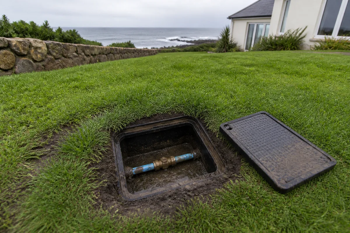 Regard d eau ouvert dans une pelouse de pavillon breton, tuyau polyethylene et raccord visibles, terre humide autour