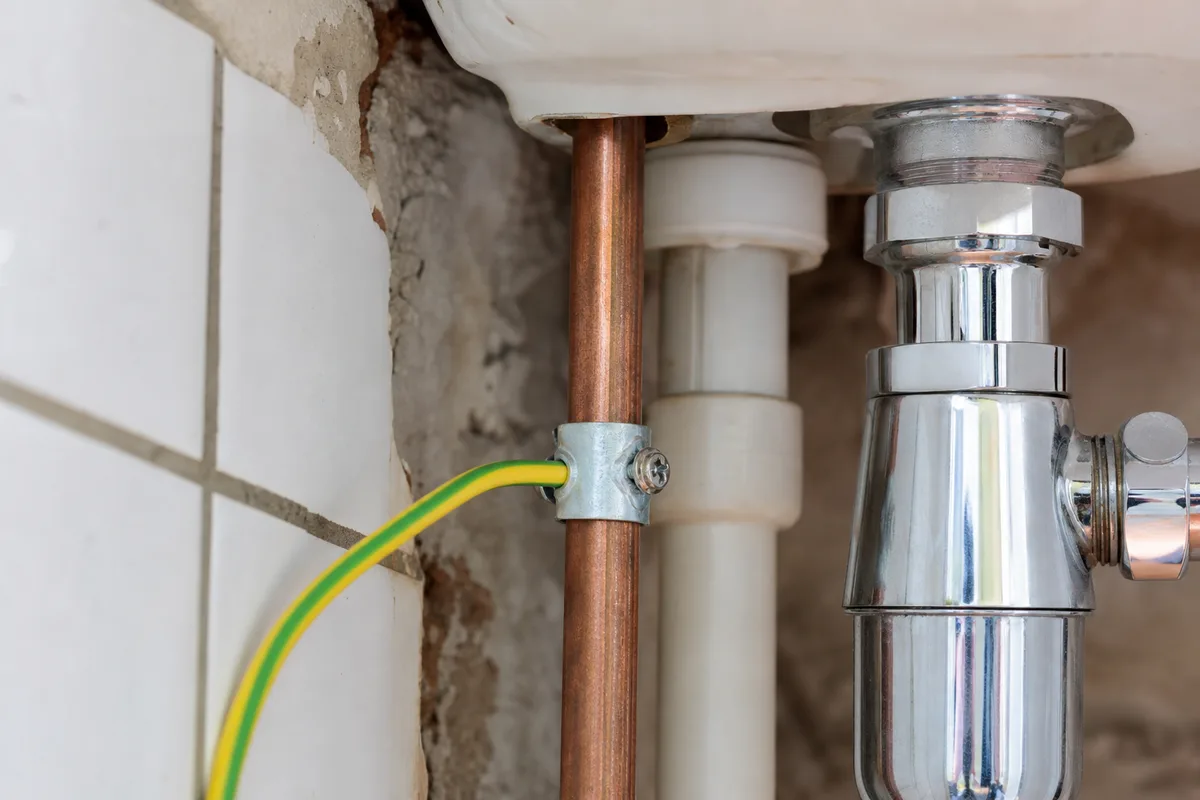 Conducteur vert et jaune de liaison équipotentielle serré sur une canalisation d&rsquo;eau en cuivre sous un lavabo