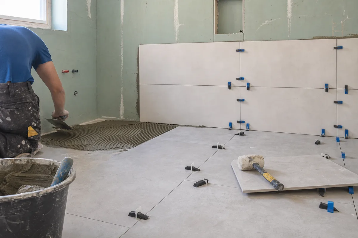 Chantier de rénovation de salle de bains avec pose de carrelage au sol et faïence murale
